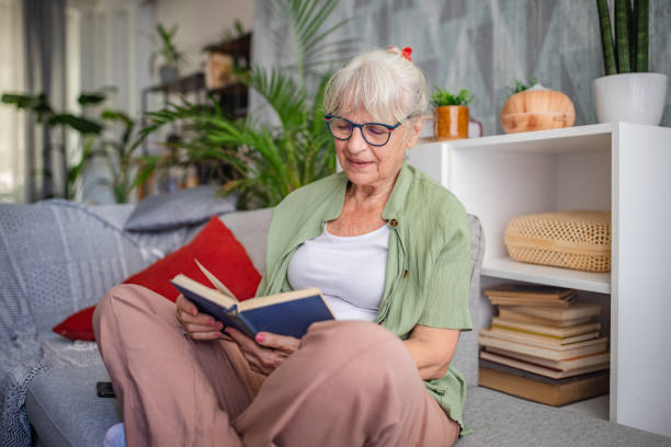 istock Elderly woman reading a book on couch at home, relaxed. 2169225437