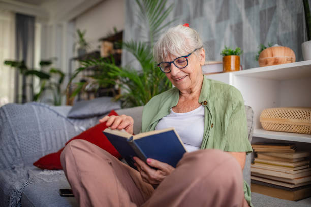 istock Elderly woman reading attentively on her gray couch. 2169225506