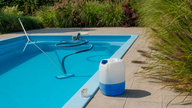 Pool cleaning hose and vacuum head with a large chemical container and water testing kit by the poolside, focusing on water quality and maintenance. stock photo