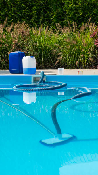 istock Pool cleaning hose submerged in a clear blue pool, with chemical containers and testing kit on the poolside, surrounded by lush greenery. 2169227650
