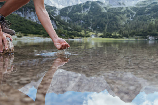 Close-up of a hand reaching down to touch the reflective surface of a serene mountain lake, capturing the tranquility of nature.