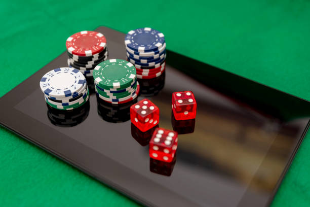 istock Stacks of Poker Chips and Red Dice on a Digital Tablet on green felt background 2169232120