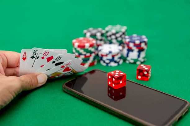 istock Hand holding poker playing cards with chips, dice, and smartphone on green felt table 2169232147