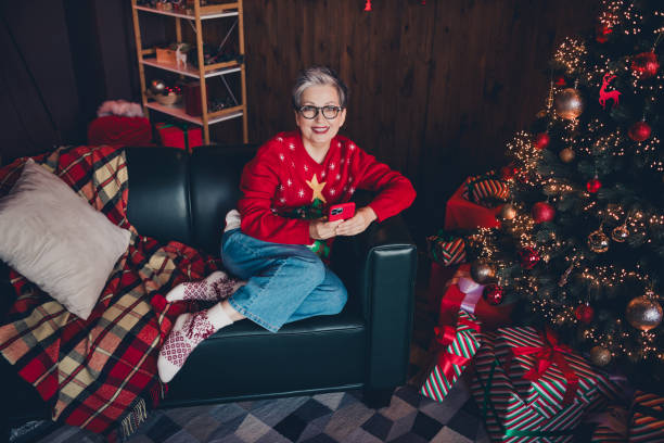 istock Full body length photo of cheerful grandmother in red pullover using smartphone at home decorated like santa claus workshop with xmas tree 2169243473
