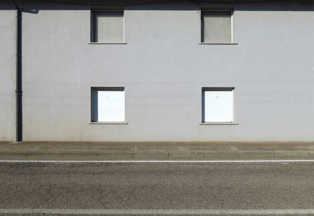 Gray plaster building with closed white shutters. Concrete sidewalk and street in front. Background for copy space.