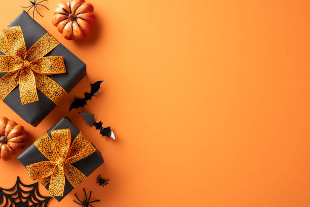 istock Top view of Halloween gifts with orange ribbon and decorations including pumpkins and bats on an orange background 2169263473