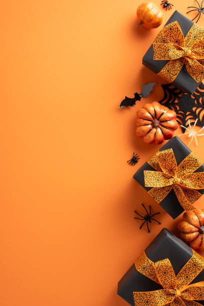 istock Halloween vertical themed presents with black gift boxes and orange ribbons surrounded by pumpkins and spooky decorations on an orange background 2169263486
