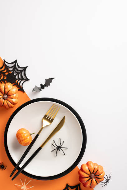 istock Halloween vertical themed table setting with small pumpkins, black and gold cutlery, and spider and bat decorations 2169263511