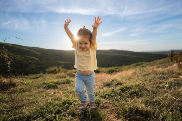 Full length of cute little girl whit raised hands running on a mountain at sunset
