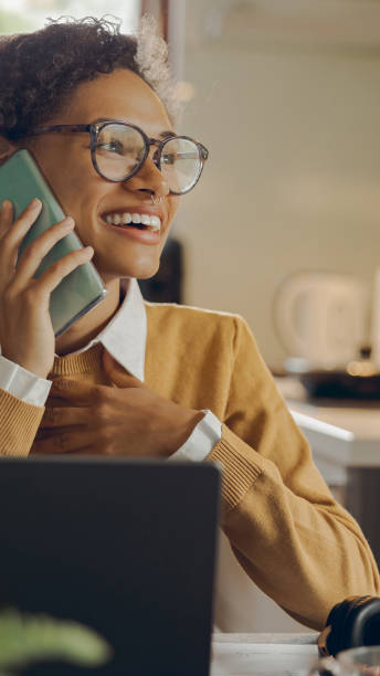 istock Female freelancer is talking phone while working on laptop from home sitting at kitchen 2169266487
