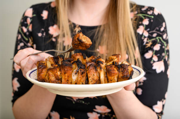 A woman holds a plate full of grilled meat pieces, morsels on a fork