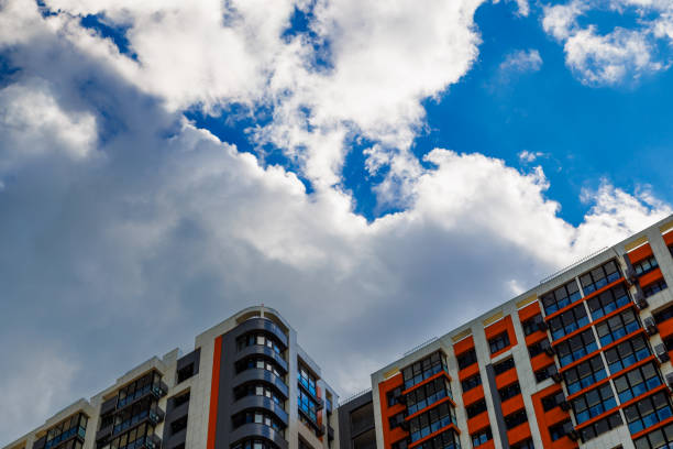 freshly built high rise apartment building on blue sky background with white clouds.
