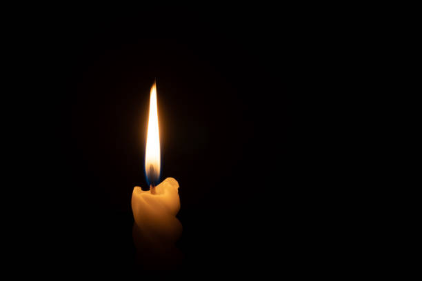 istock A single burning candle flame or light glowing on a spiral white candle on black or dark background on table in church for Christmas, funeral or memorial service with copy space 2169284330