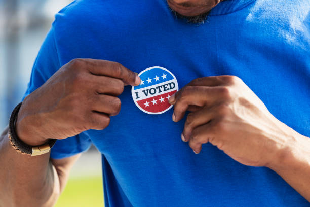 Cropped view of man putting I Voted sticker on shirt Cropped view of a mature man in his 40s putting an I VOTED sticker on his shirt. He is African-American and Native American. early voting stock pictures, royalty-free photos & images