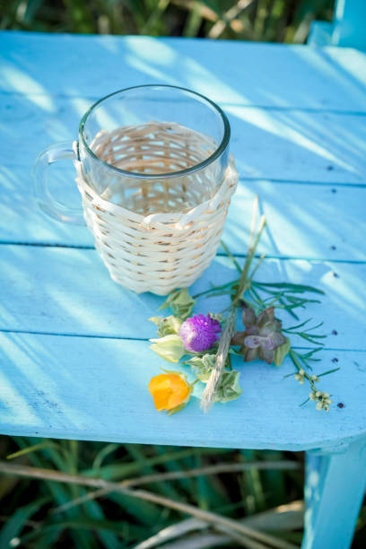 Glass cup lined with wicker, on a light blue chair in the field.