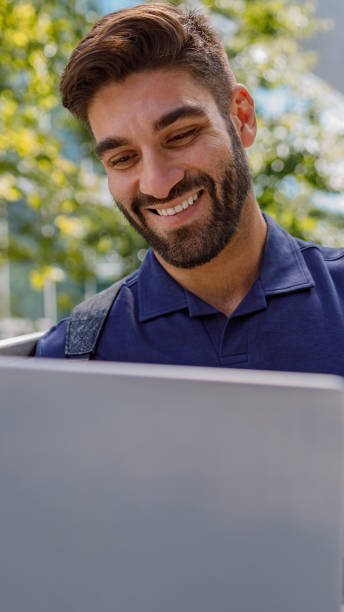 istock Positive male freelancer working on laptop standing on skyscrapers background. Distance work concept 2169341900
