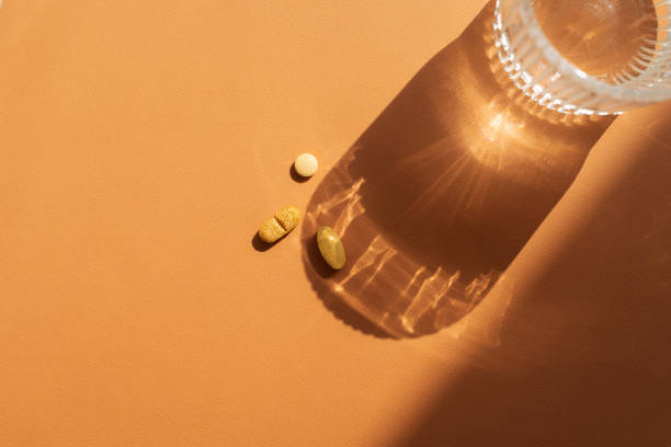 istock A clear glass of water casting a shadow on orange surface, along with several orange pills placed nearby. Strong shadow and  reflective effect through the glass, top view 2169347707