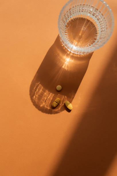istock A clear glass of water casting a shadow on orange surface, along with several orange pills placed nearby. Strong shadow and  reflective effect through the glass, top view 2169347741
