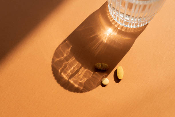 istock A clear glass of water casting a shadow on orange surface, along with several orange pills placed nearby. Strong shadow and  reflective effect through the glass, top view 2169348259