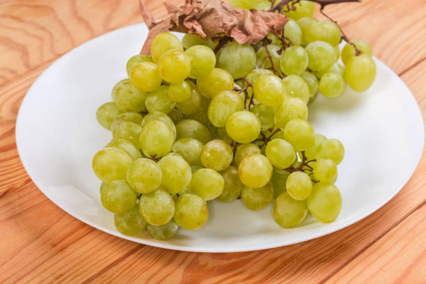 Clusters of the ripe white sultana grape with dry vine leaf on a white dish on a wooden rustic table, side view close-up in selective focus