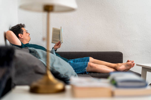 A man reclines comfortably on a couch, deeply engrossed in a book.