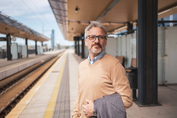 istock Mature businessman standing on a train station platform, looking thoughtful and ready for a commute. He holds a jacket over his arm and is dressed in business casual attire, exuding confidence and experience. 2169359570