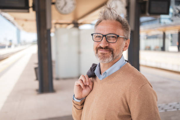 istock Confident mature man with glasses waiting at a train station while carrying his jacket. Perfect for concepts of business commuting, professionalism, and daily routine of a senior professional. 2169359571