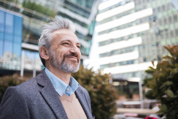 istock A mature businessman confidently smiling while standing outdoors in a modern urban environment. The photo captures a positive and successful professional demeanor, reflecting optimism and a strong presence. 2169359581