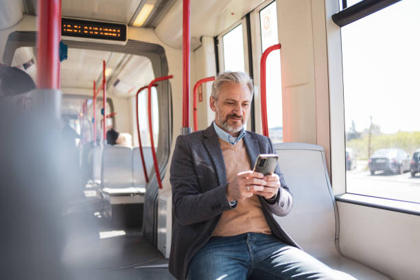 istock A mature man riding on a public train, working remotely from his smartphone. The image captures the modern-day business commuter in a casual setting, highlighting the concept of remote work and flexibility. 2169359582