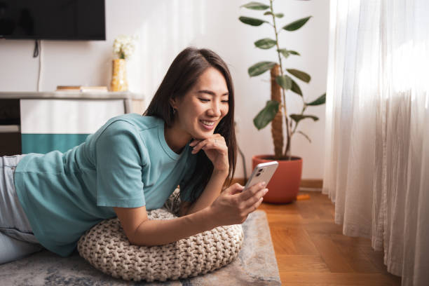 istock Asian woman lying on floor, using phone, and smiling 2169359590