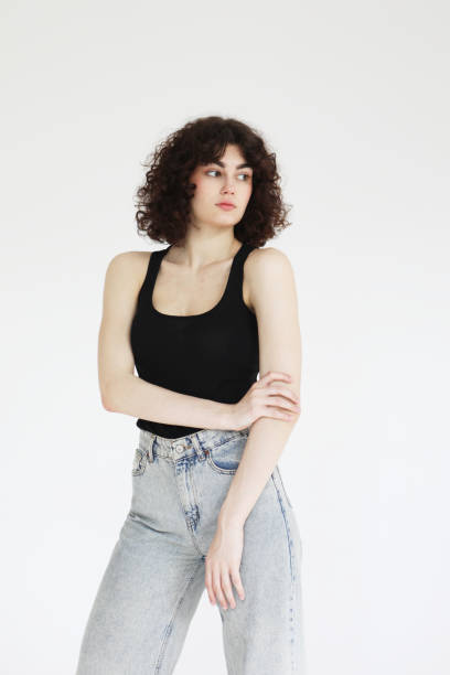 istock young curly woman in a black tank top posing over light grey background. 2169360650