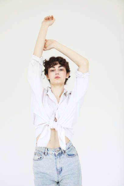 Young curly female model in jeans and white shirt posing on white background.