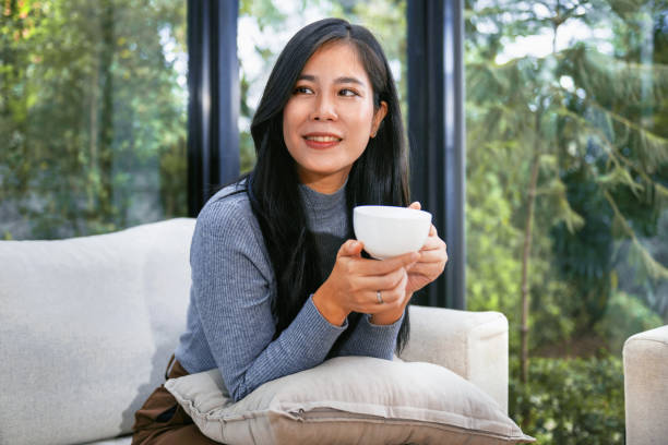 istock woman is sitting on a couch with a white cup in her hand 2169363677