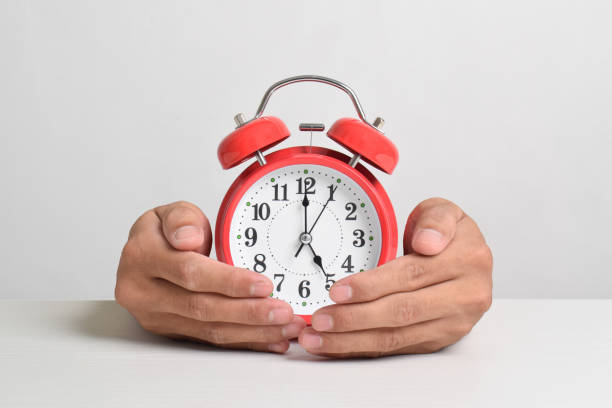 istock man holding red alarm clock in the hands on white background 2169370053