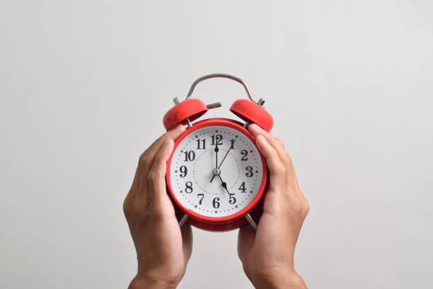 istock Male hand holding red alarm clock on white background 2169370108