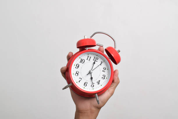 Vintage red alarm clock in hand. Round red alarm clock isolated on white background shows 5 am