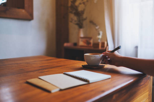 istock Closeup image of a hand holding a cup of coffee while writing on notebook on the table 2169383286
