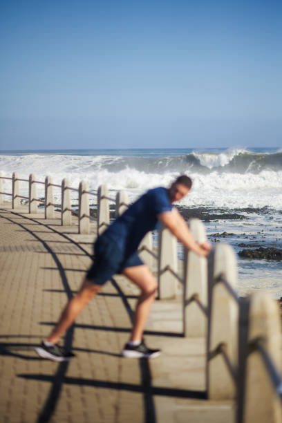 Defocussed athlete stretching on promenade with wave in focus Cape Town South Africa