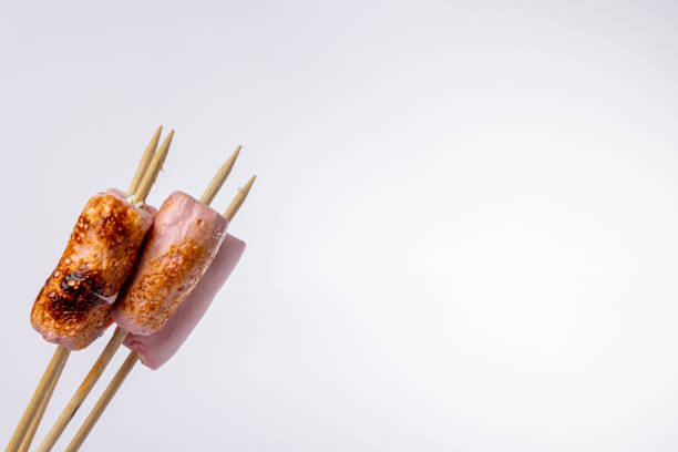 Close-up view of skewers with marshmallows, toasted to a golden brown, angled to the left. The horizontal photo is set against a white background, emphasizing the crisp, toasted surface of the marshmallows
