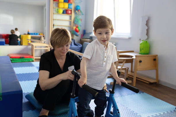 istock Young boy with cerebral palsy practices using a walker with guidance from his physical therapist in room for physical therapy 2169405271