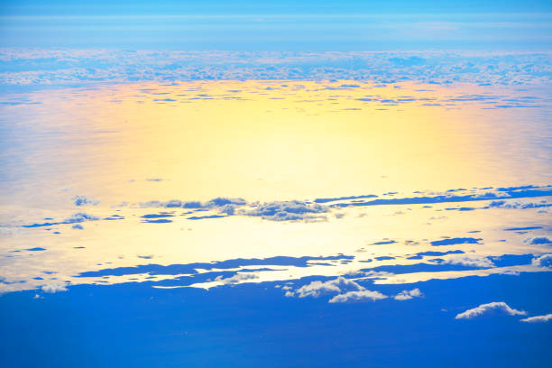 Aerial view showcasing the vast ocean meeting the sky, captured from an airplane window during flight. Flying over the clouds and ocean in the twilight