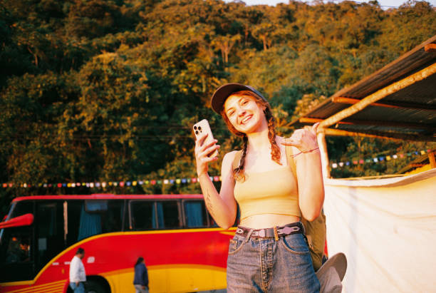 Cheerful woman  using smartphone and showing shaka gesture while waiting for the bus in summer shot on camera film
