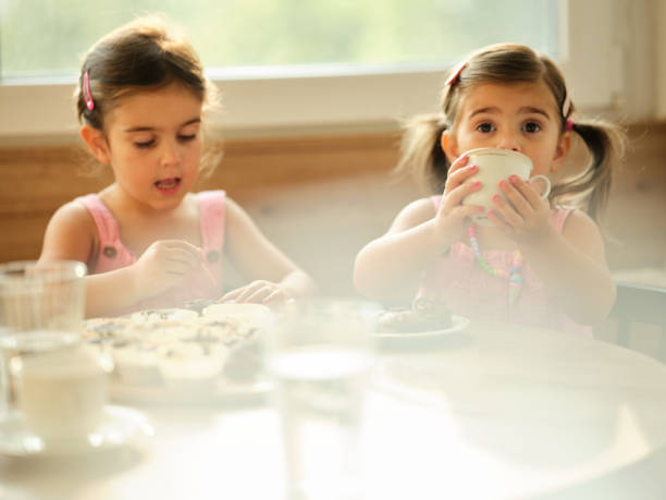 Elementary Pupils Enjoying Healthy Lunch In Cafeteria Sitting Down Smiling At Camera
