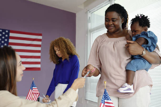 African American woman visiting voting centre with her baby and taking bulletin to vote