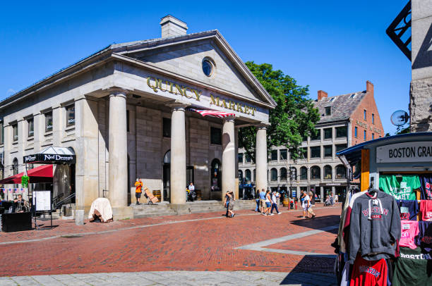 Boston, Massachusetts, USA- August 12 2024-Groups of tourists enter the front doors of Boston's Quincy Market as colorful   Boston sweatshirts   are being sold from a nearby kiosk.