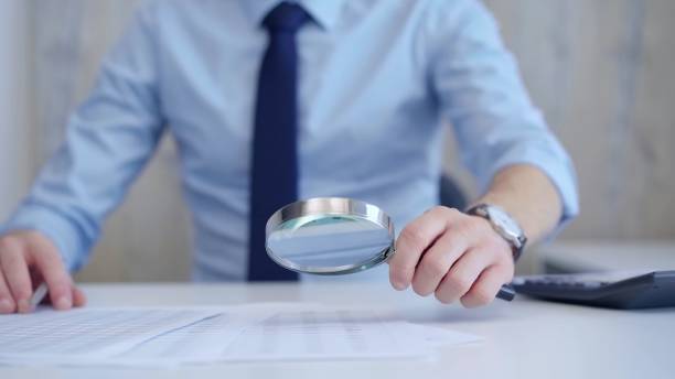 istock Businessman is carefully examining financial documents with a magnifying glass, highlighting the importance of thorough analysis in business. Audit and taxes 2169442669