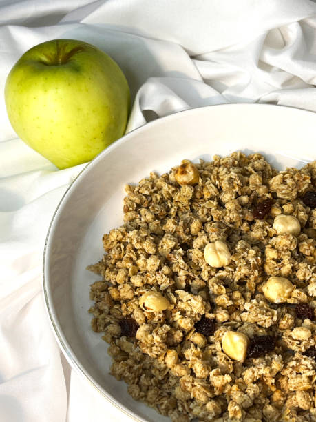 istock Granola with nuts and raisins in a white plate with apple close-up on a white textile background. 2169446936