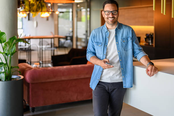 istock Portrait of confident male engineer smiling and texting over smart phone while standing in office 2169448146