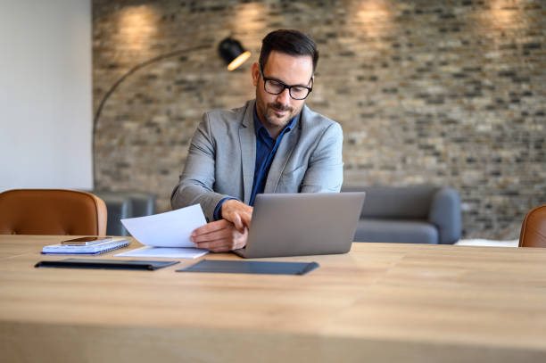 istock Male financial advisor analyzing with glasses reports over laptop while working at desk in office 2169448243