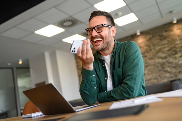 istock Low angle view of inspired entrepreneur laughing while talking over phone speaker at desk in office 2169448299